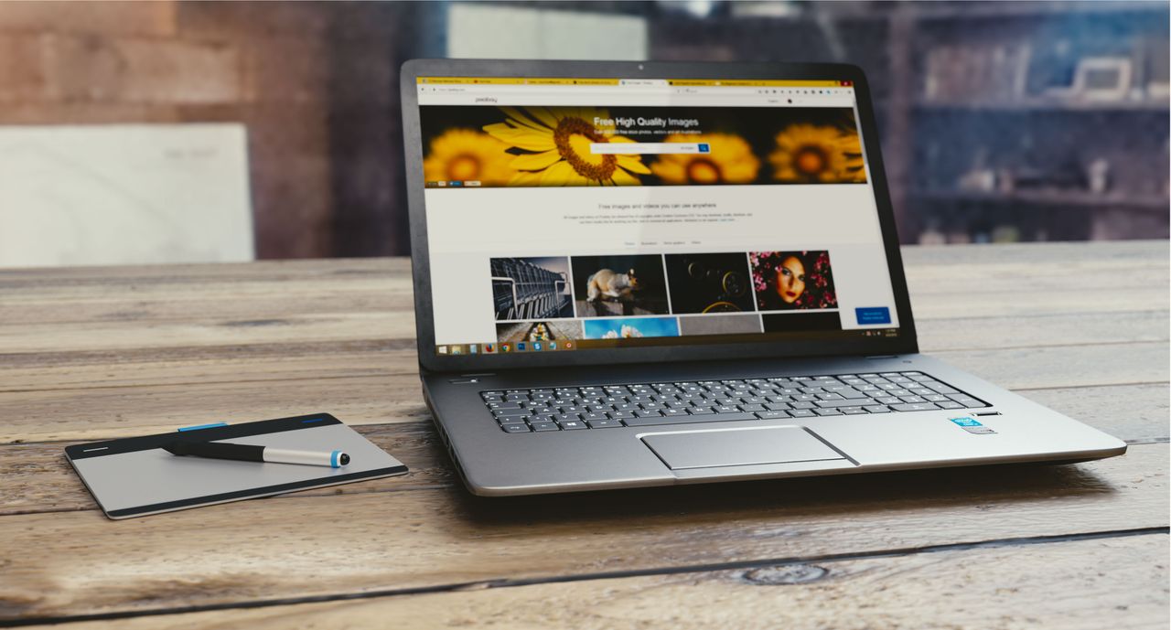 Home Laptop with open webpage on wooden desk, accompanied by tablet and pen, representing digital work setup.