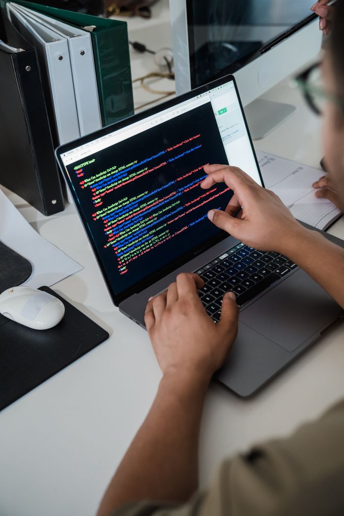 Services Close-up of a programmer pointing at a colorful code script on a laptop in an office setting.